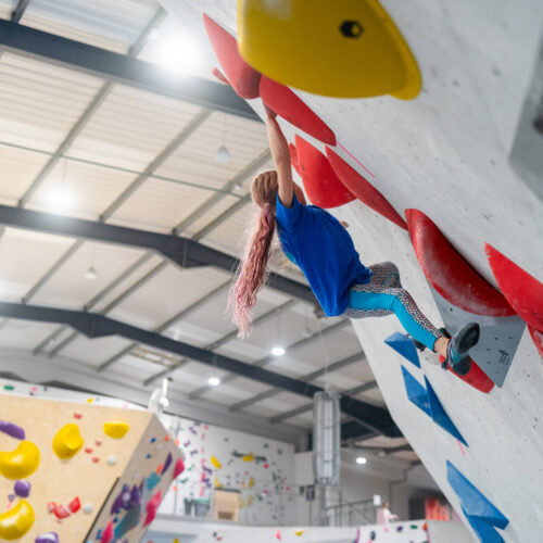 Child climbing steep indoor bouldering wall at Flashpoint Easton using large red holds on an overhang route