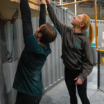 Instructor pointing to fingerboard holds while a climber practices grip training on a hangboard inside Flashpoint Easton