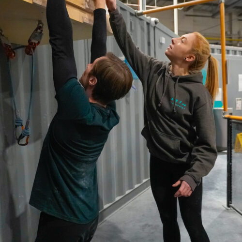 Instructor pointing to fingerboard holds while a climber practices grip training on a hangboard inside Flashpoint Easton