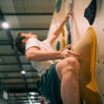 Man climbing up a bouldering wall, reaching high while holding a large orange volume at Flashpoint Easton