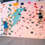 Boy and woman climbing on a bouldering wall with colourful holds and a large lightning bolt graphic at Flashpoint Easton