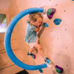 Young girl gripping colourful holds while climbing around the circular feature in the kids’ area at Flashpoint Easton