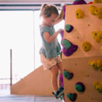 Toddler carefully placing her foot on purple and green holds in the junior climbing area at Flashpoint Easton