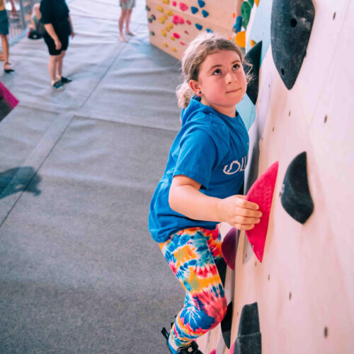 Young climber reaching for a pink hold on the kids’ wall at Flashpoint Easton