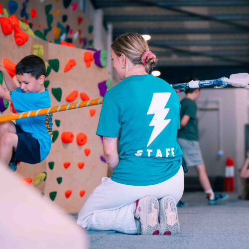 Boy climbing on the kids’ wall while a Flashpoint Easton staff member kneels nearby for support