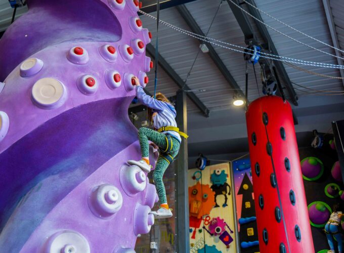 Girl wearing a harness climbs a purple feature wall with round holds in the kids’ climbing area at Flashpoint Easton